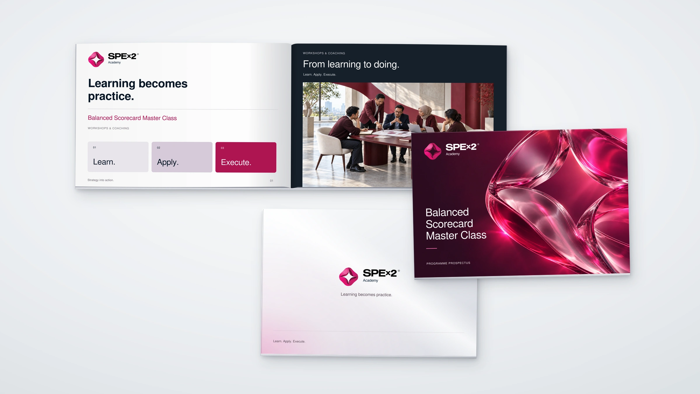Academy prospectus in a near-overhead three-piece studio composition: an open landscape spread, a raspberry glass front cover and a pale silver back cover, all with matching page sizes and original Academy logos.