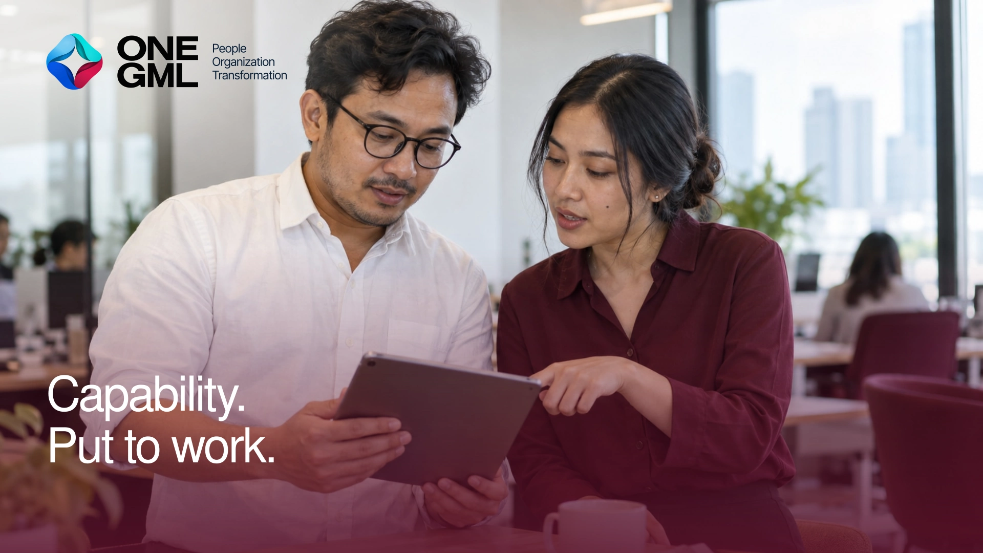 Two Indonesian professionals reviewing a tablet in a bright office, with burgundy clothing and furniture.